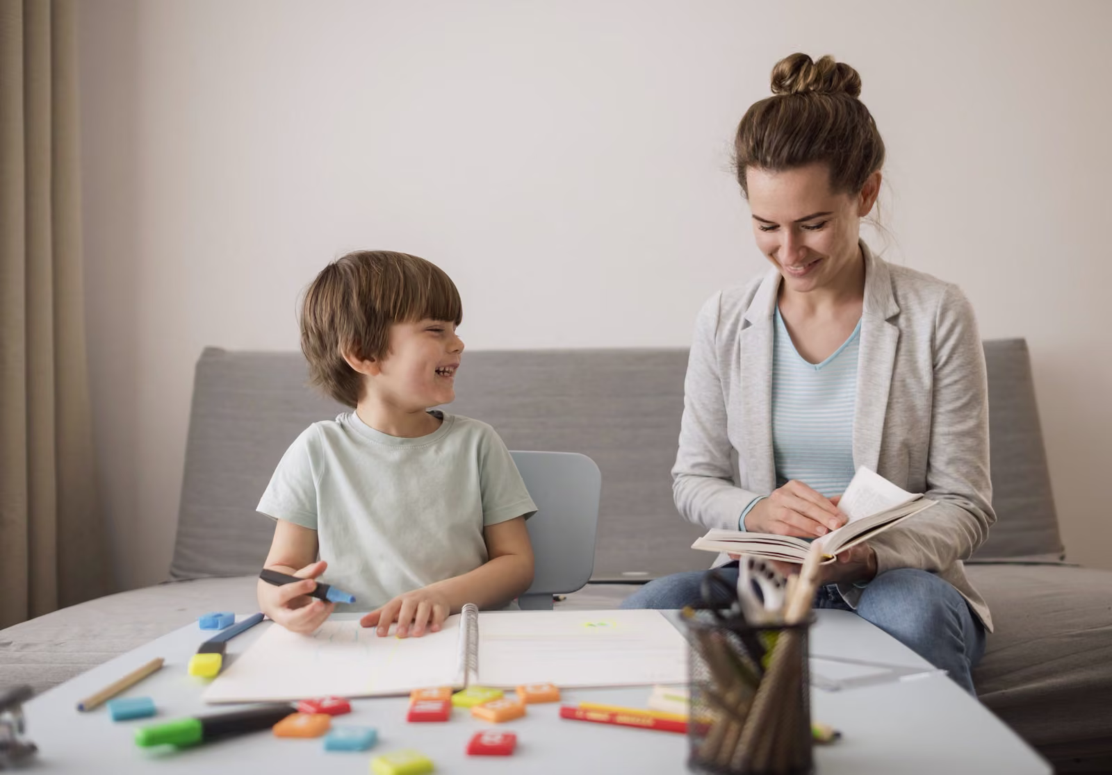 A practitioner and a young boy working together at a table in a bright living room