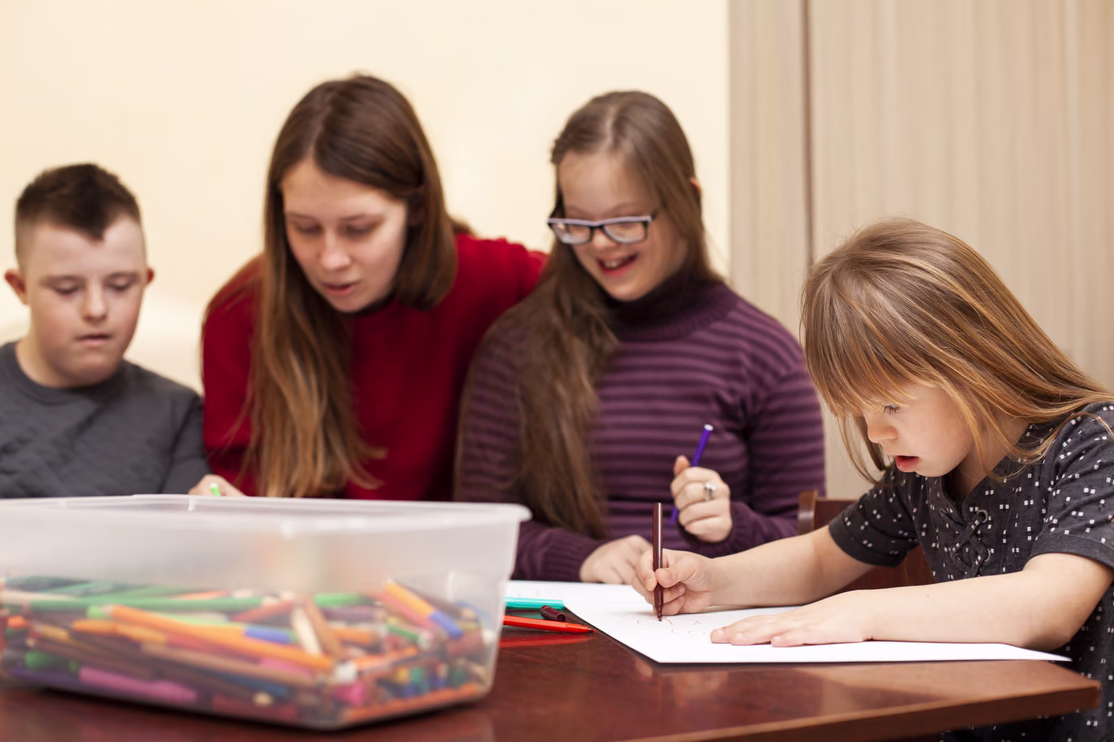 A group of young people drawing together at a table with an adult helping