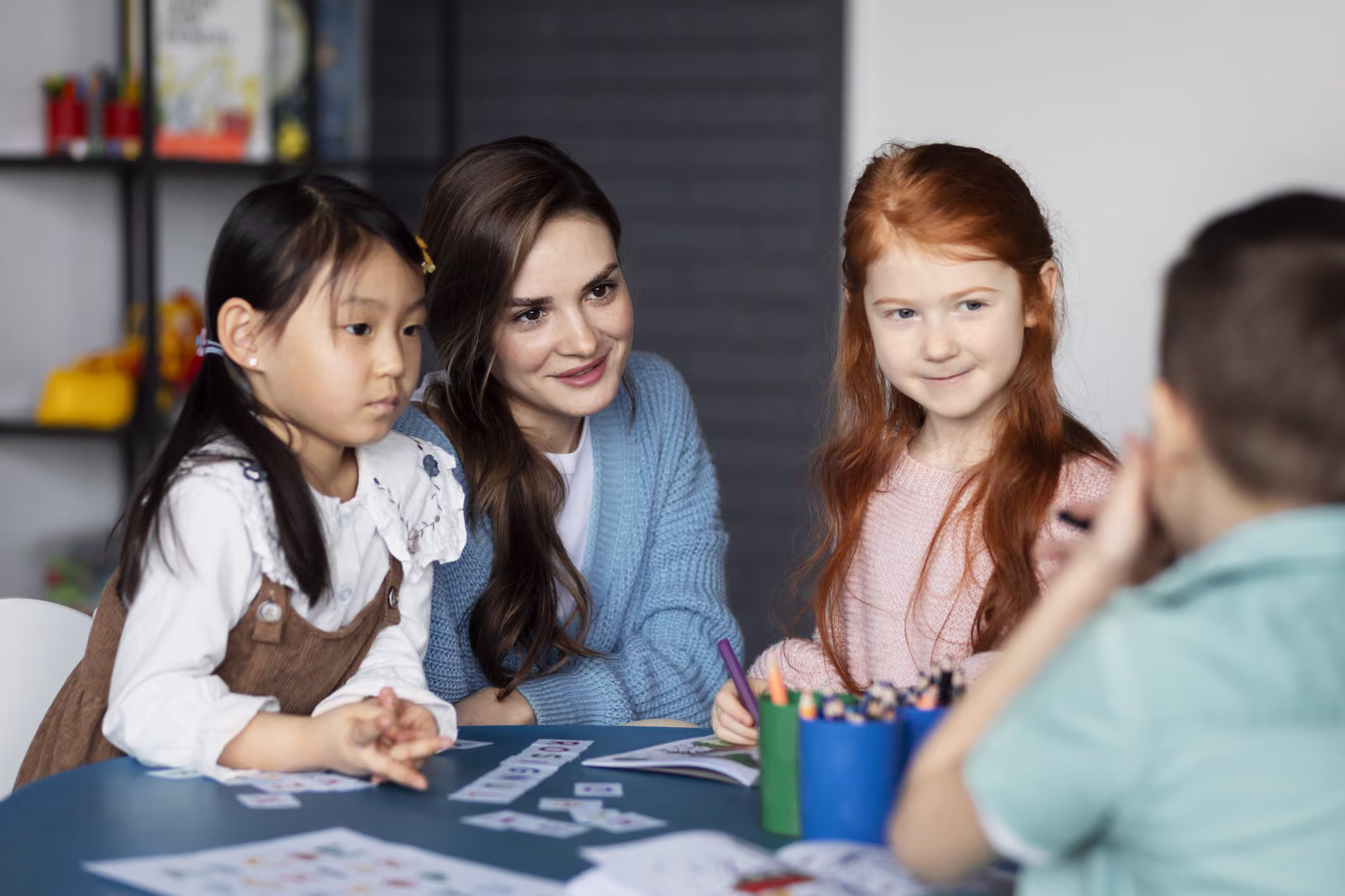 A teacher and children sitting together at a table with drawing materials